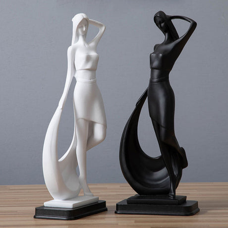 Two abstract sculptures, one white and one black, on a wooden surface with a gray wall background.
