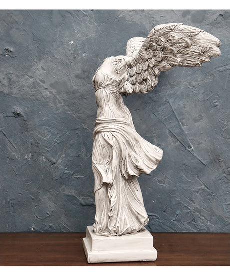 Statue of a winged figure against a textured gray wall