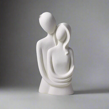 White ceramic sculpture of two abstract figures embracing on a gray surface with a dark background