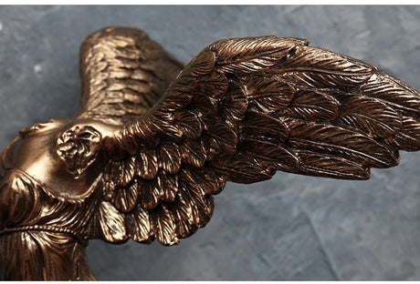 Bronze sculpture of an angel with outstretched wings on a gray background