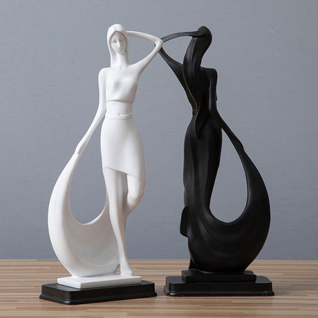 Two abstract sculptures, one white and one black, on a wooden surface with a gray background.