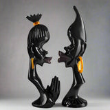 Black and gold sculpture of two figures on a white background