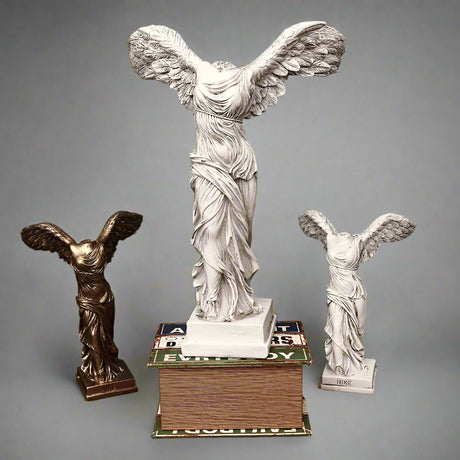 Three winged statue figurines on a textured surface with a blue wall background