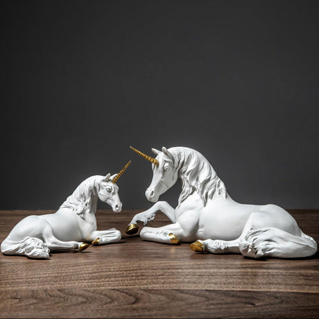 Two white unicorn figurines with gold hooves and horns on a wooden surface.