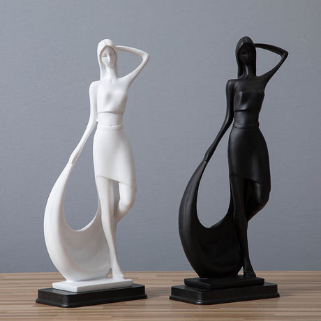 Two abstract statues, one white and one black, on a wooden surface with a gray background.