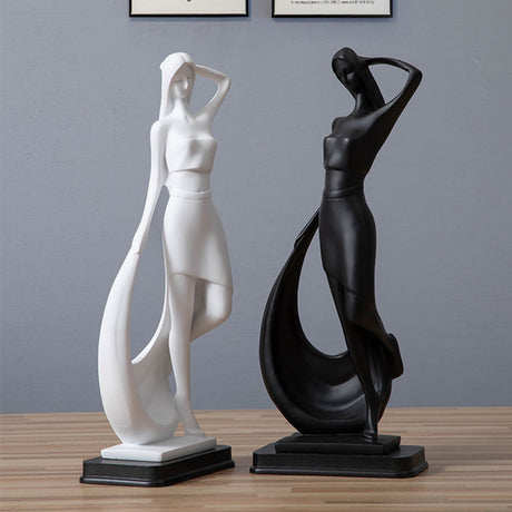 Two abstract sculptures, one white and one black, on a wooden surface with a gray wall background.